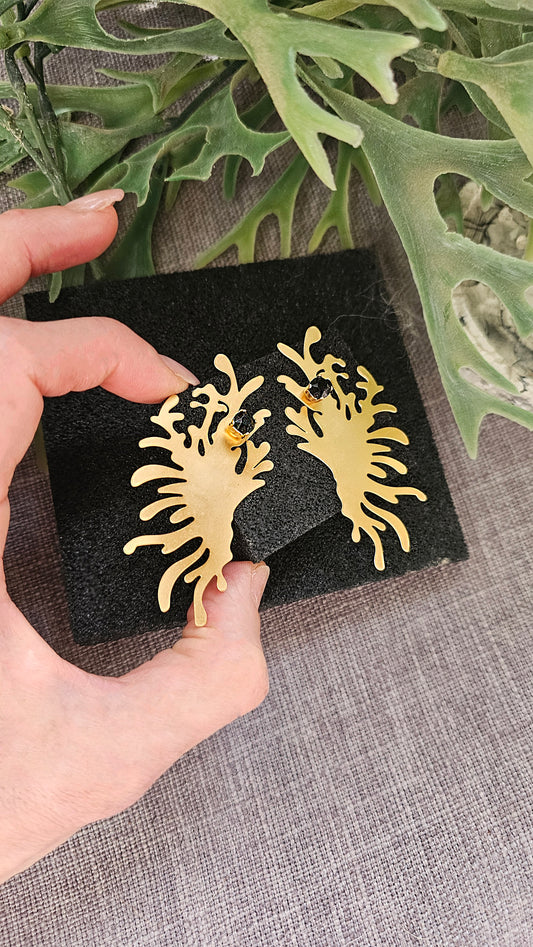 a person is holding a pair of gold earrings