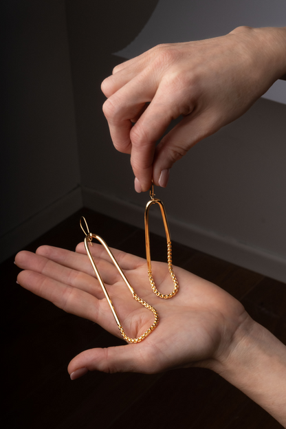 a pair of hands holding a pair of gold earrings
