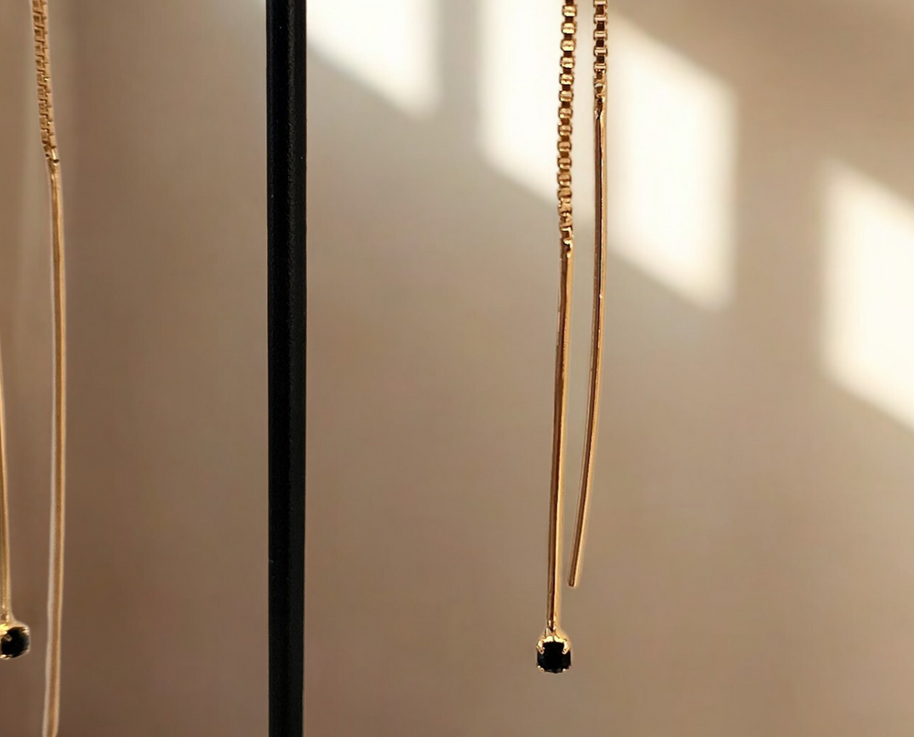 Gold necklace with black beads on a black stand against a beige wall.
