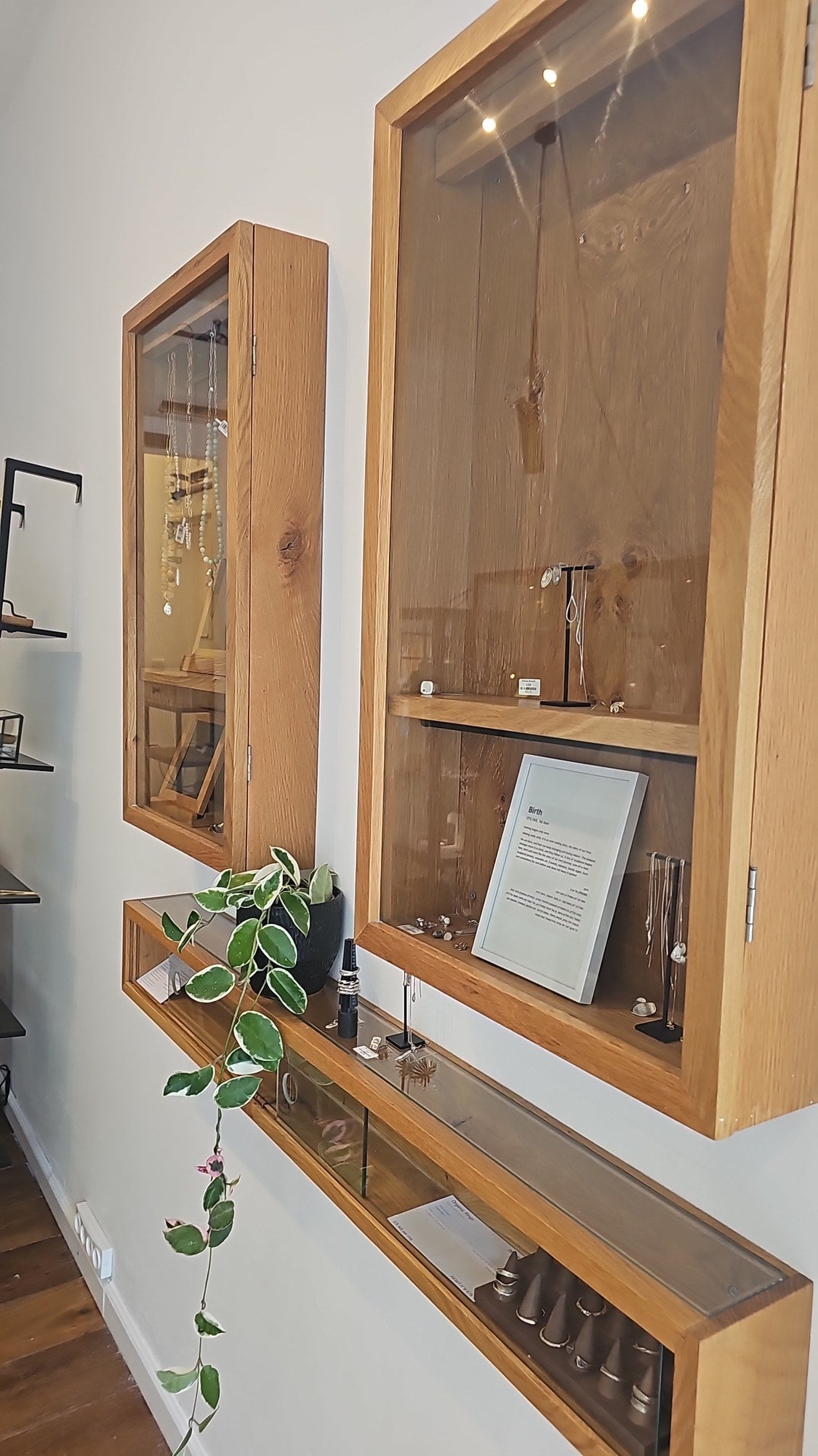 Oak wall cases with handmade OTILYAS jewelry and a trailing plant